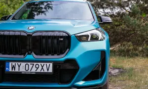 Turkusowy BMW X1 2024 z czarnym grillem i emblematem M, gotowy na przygodę w otoczeniu natury.