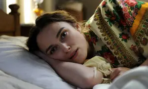 Eine Frau liegt im Bett, ihr Blick wirkt nachdenklich, vielleicht ein Zeichen für psychische Symptome. Ihr Kopf ruht auf ihrem Arm, bedeckt von einem bunten Tuch.