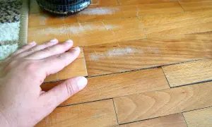 Mano sul parquet graffiato, un problema comune per chi vuole sapere come togliere strisciate scarpe dal parquet.