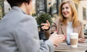 Dwie kobiety rozmawiają przy stoliku, pijąc kawę. Widać, że łączy je przyjaźń w pracy, pełna szczerych rozmów i uśmiechów.
