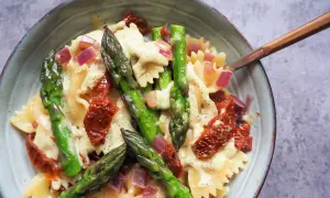 Makaron farfalle z zielonymi szparagami, suszonymi pomidorami i czerwoną cebulą w kremowym sosie.