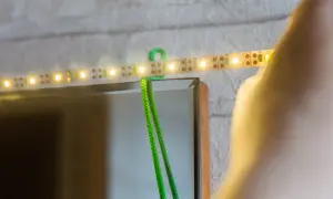 Montaż taśmy LED za lustrem: zielony kabel i świecące diody tworzą subtelne oświetlenie.