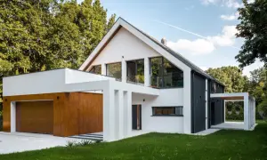 Nowoczesny, biało-czarny dom z drewnianą bramą garażową, otoczony zielenią.