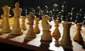 Białe figury szachowe, w tym król, hetman i goniec, ustawione na szachownicy. Ciemne figury w tle.