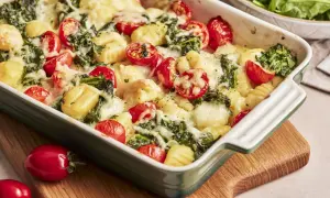 Gnocchi Spinat Auflauf mit Kirschtomaten und geschmolzenem Käse in einer grünen Auflaufform.