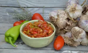 Un bol de piperade basque aux poivrons verts, tomates et oignons, avec des gousses d'ail et des herbes sur fond de bois.
