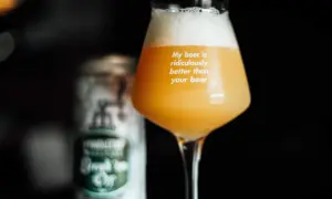 Bicchiere con birra neipa dal colore dorato e schiuma abbondante. Sul vetro la scritta "My beer is ridiculously better than your beer". Sullo sfondo una lattina sfocata.
