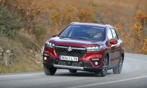 Röd Suzuki S-Cross kör på en kurvig väg i höstlandskap. En man med solglasögon kör bilen under en suzuki s-cross test.