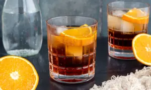 Ein erfrischender Americano Cocktail mit Eis und Orangenscheiben, daneben eine Karaffe Wasser und frische Orangen.