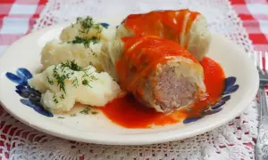 Gołąbki z kapusty włoskiej, podane z purée ziemniaczanym i polane sosem pomidorowym, ozdobione koperkiem.
