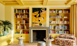 Ein Wohnzimmer in einem gelben Farbrausch, mit Bücherregalen, einem Kamin und einem bunten Sofa.