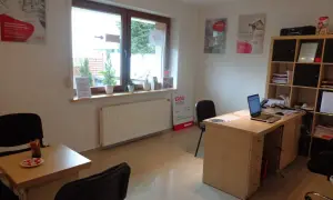 Biuro z biurkiem, laptopem, krzesłami i oknem.