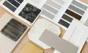 Próbki materiałów do wnętrz: czarny konglomerat, jasne płytki, białe drzwi i tkaniny.