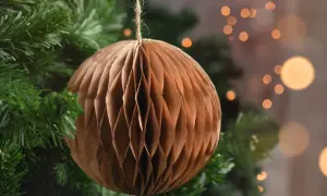Brązowa, papierowa ozdoba choinkowa w kształcie kuli wisi na gałęzi choinki.