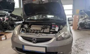 Srebrna Honda Jazz z otwartą maską, widoczny silnik i akumulator. Wymiana żarówki Honda Jazz w warsztacie.