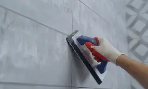 Hand in glove using a trowel for repairing grouting between light grey tiles.