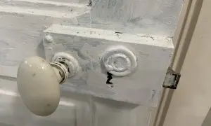 Poignée de porte ancienne recouverte de peinture blanche écaillée. Le mécanisme de serrure est visible, prêt à enlever peinture sur poignée de porte.