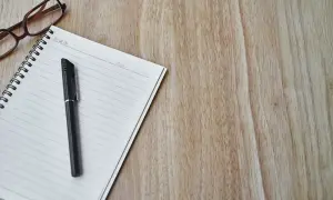Okulary, notatnik i długopis na drewnianym blacie. Taka kombinacja sugeruje, że opinia z poradni jest ważna i wymaga przemyślenia.