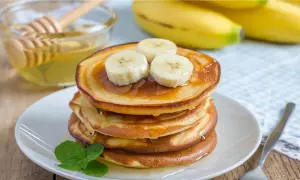 En stapel gyllene bananpannkakor toppas med bananskivor och ringlad honung. Ett enkelt bananpannkaka recept för en härlig frukost.