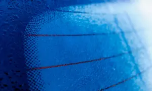 Gotas de agua sobre los **filamentos transversales de la luneta trasera** de un coche, creando un patrón abstracto azul.