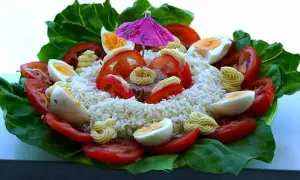 Salade de riz thon festive, garnie d'œufs durs, tomates, mayonnaise et d'un petit parasol rose. Un délice coloré !