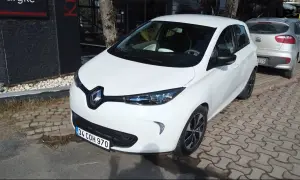 Białe Renault Zoe stoi zaparkowane na chodniku z kostki brukowej.