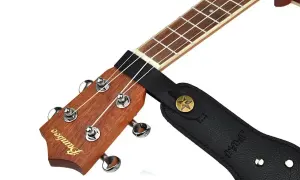 Czarny pasek do gitary zaczepiony na gryfie ukulele. Pokazuje, jak zacząć grać, gdy masz już zamontowany pasek.