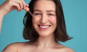 Uśmiechnięta kobieta z piegami aplikuje serum. Czy ceramidy można łączyć z witaminą C dla zdrowej cery?