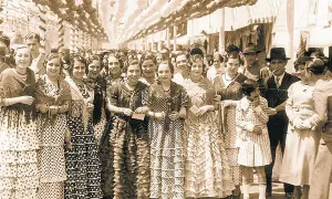 Grupo de mujeres y niñas con trajes de volantes y lunares, evocando el origen del traje de flamenca en una feria antigua.