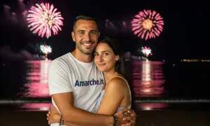 Coppia abbracciata sulla spiaggia con fuochi d'artificio rosa e verdi sullo sfondo. Un'idea perfetta per cosa fare a Ferragosto.