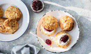Nybakade scones med mandelflagor, grädde och sylt på en tallrik. En härlig fika!