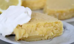En bit kladdkaka med citron, toppad med vispad grädde. En perfekt citron kladdkaka för fikat.