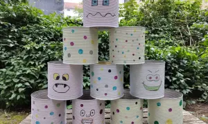 Kreatives Recycling mit Kindern: Dosen-Monster-Turm im Garten. Bunte Punkte und lustige Gesichter machen aus alten Konserven ein Spiel.