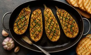 Quatre moitiés d'aubergine au four, grillées et parsemées de persil frais, dans un plat ovale. Des toasts grillés et de l'ail complètent ce plat savoureux.