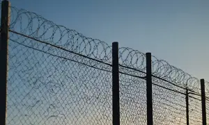 Ogrodzenie z siatki z drutem kolczastym na górze, przypominające o przepisach dotyczących bezpieczeństwa.