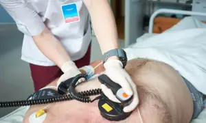 Ratownik medyczny wykonuje kardiowersję pacjentowi leżącemu w łóżku szpitalnym.