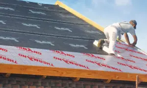 Pracownik montuje izolację nakrokwiową na dachu, układając warstwy materiału termoizolacyjnego.