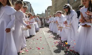 Dziewczynki w bieli sypią płatki kwiatów na ulicy. To piękny widok podczas procesji Bożego Ciała, święta upamiętniającego Ostatnią Wieczerzę.