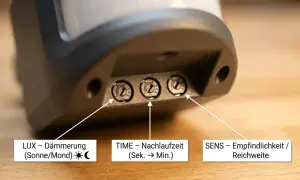 Nahaufnahme von drei Einstellrädern an einem Bewegungsmelder: LUX (Dämmerung), TIME (Nachlaufzeit) und SENS (Empfindlichkeit/Reichweite). So lässt sich der Bewegungsmelder einstellen.
