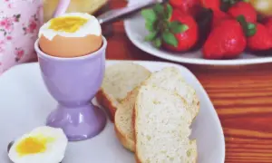 Jajko na miękko w fioletowej kieliszkowej podstawce, obok kromki chleba i łyżeczka z połówką jajka. Czas do gotującej wody minął idealnie.