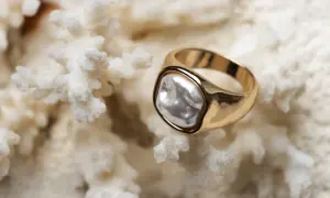 Anillo de oro amarillo con perla irregular sobre coral blanco. La diferencia entre oro blanco y oro amarillo es evidente en su brillo.