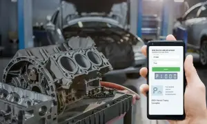 Mechanik sprawdza kod błędu DTC P1000 Ford na telefonie, obok rozebranego silnika w warsztacie.