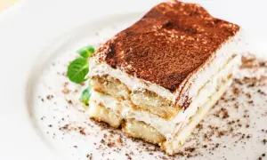 Une part de tiramisu mascarpone, aérienne et gourmande, saupoudrée de cacao, avec une touche de menthe fraîche.