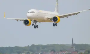 Samolot hiszpańskich linii lotniczych Vueling z żółtymi gondolami silników zbliża się do lądowania nad malowniczą miejscowością.