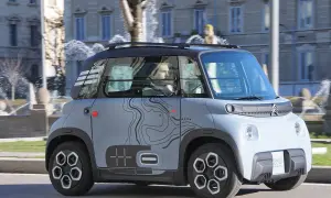 Citroën Ami, un veicolo elettrico compatto, sfreccia con la sua velocità massima in città, con uno sfondo di fontane e palazzi.