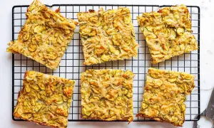 Sechs rechteckige Stücke einer gebackenen Zucchinipfanne mit gelben Zucchinischeiben auf einem schwarzen Gitter.