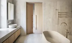 Elegancka, ciepła beżowa łazienka z wolnostojącą wanną, umywalką nablatową i drewnianymi drzwiami.