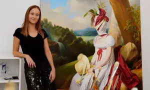 Ewa Juszkiewicz z rodziną na tle swojego obrazu. Artystka w czarnej koszulce i spódnicy ubrudzonej farbą, obok płótna z tajemniczą postacią.