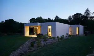 Modernos modelos de casas unifamiliares con fachadas de baldosas grises, iluminadas al anochecer.