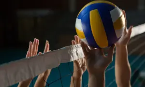 Piłka do siatkówki tuż nad siatką, ręce graczy próbują ją odbić. Ile minut trwa mecz? Zależy od wyniku!